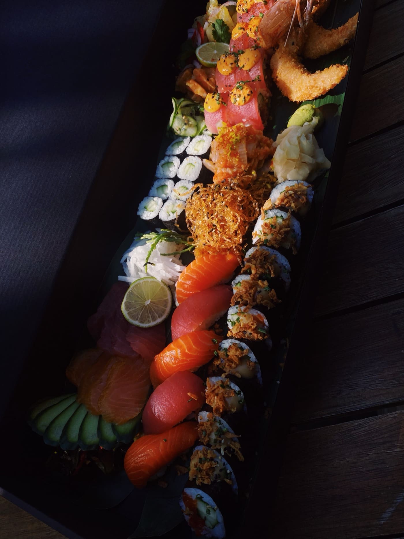 Lange schwarze Sushi-Platte mit Nigiri, Maki, Sashimi, Tempura-Garnelen und Limette