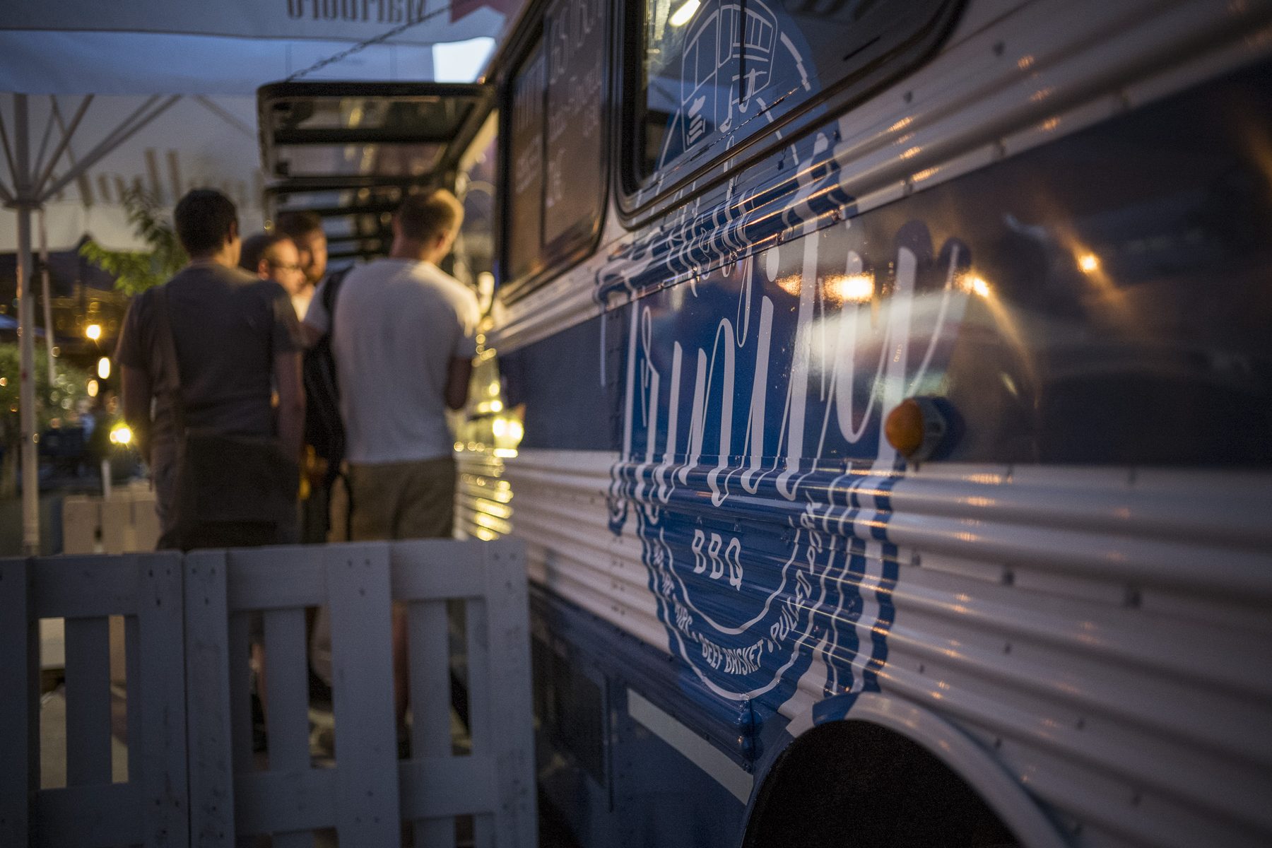 Der beleuchtete Foodtruck am Abend, Gäste stehen im Lichterschein davor